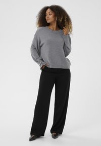 Suéter gris de punto con hombros caídos, escote redondo y dobladillo acanalado, combinado con pantalones de pierna ancha negros y zapatos de punta.