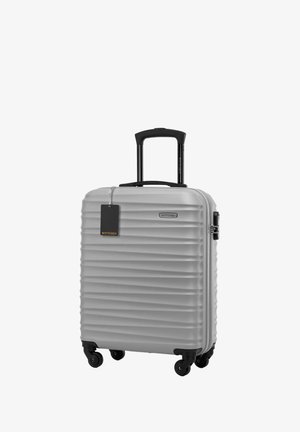 Valise rigide argentée avec des rainures verticales, poignée rétractable noire, poignée de transport supérieure et quatre roues pour la mobilité.