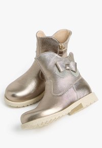 Bottines dorées métalliques avec une fermeture éclair sur le côté, un nœud décoratif à l'extérieur et une semelle texturée. Fini en cuir lisse, design décontracté.