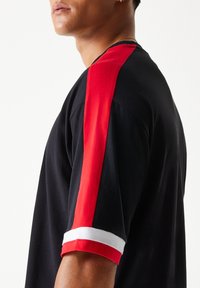 Fekete póló piros és fehér csíkos ujjakkal. Puha anyagból, laza szabással, lekerekített nyakkivágással. Egyszerű kialakítás.