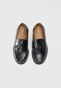 Black leather loafers with braided detailing, tassels on the front, and a smooth finish. The interior features a brown insole with branding.