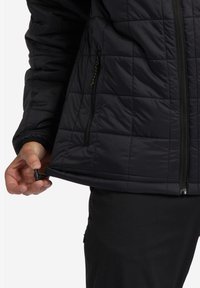 Schwarze gesteppte Jacke mit Reißverschluss vorne und zwei seitlichen Taschen. Sie verfügt über einen elastischen Zug am Saum, eine glatte Textur und ein gepolstertes Design für Wärme.