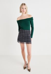 Grønn off-the-shoulder topp med lange ermer, parret med et svart og hvitt rutete miniskjørt og leopardmønstrede spisse hæler.