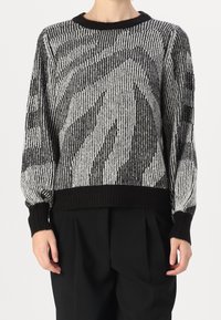Svartvit tröja med randigt mönster, stickade muddar och nederkant samt en avslappnad passform. Tillverkad av texturerat stickat material.