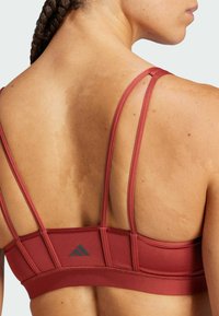 Sujetador deportivo de color marrón oscuro con tirantes finos y espalda reforzada, que presenta una superficie texturizada y un pequeño logotipo gris en la banda.