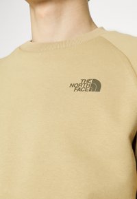 Sudadera beige con cuello redondo acanalado y mangas raglán. Presenta un pequeño logo oscuro en el pecho. Material suave de mezcla de algodón.