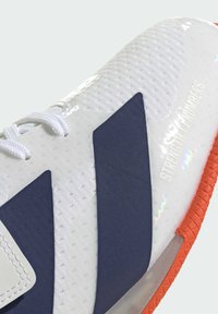 Hvide sneakers med marinefarvede accenter, struktureret mesh-overdel, glatte, blanke sektioner, orange gummisål og tekstdetalje med "Strength in Numbers".