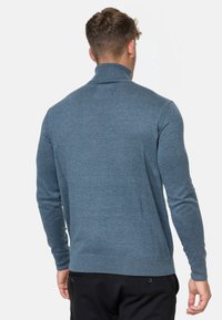 Suéter azul de manga larga con cuello alto, puños y dobladillo acanalados. Tela suave con un acabado texturizado, adecuado para combinar en capas.