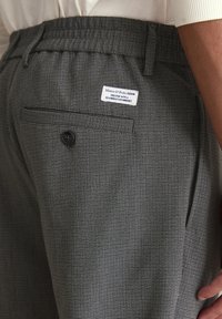 Grijze gemusterde broek met een textuurstof, voorzien van een achterzak, knoopsluiting en een merklabel op de tailleband.