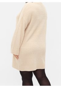 Beżowy, oversize'owy sweter z dzianiny o fakturowanej powierzchni, z długimi rękawami, ściągaczami na mankietach i dole, sięgający do połowy uda.