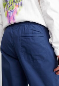 Pantaloni elasticizzati blu navy con vita elasticizzata, dotati di una tasca posteriore, realizzati in tessuto liscio con una leggera lucentezza e dettagli di cucitura minimi.