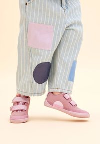 Roze sportieve schoenen met twee klittenbandsluitingen, gecombineerd met blauw gestreepte broek met lichtpaarse en donkerblauwe vlekken. Glad stoffen textuur.