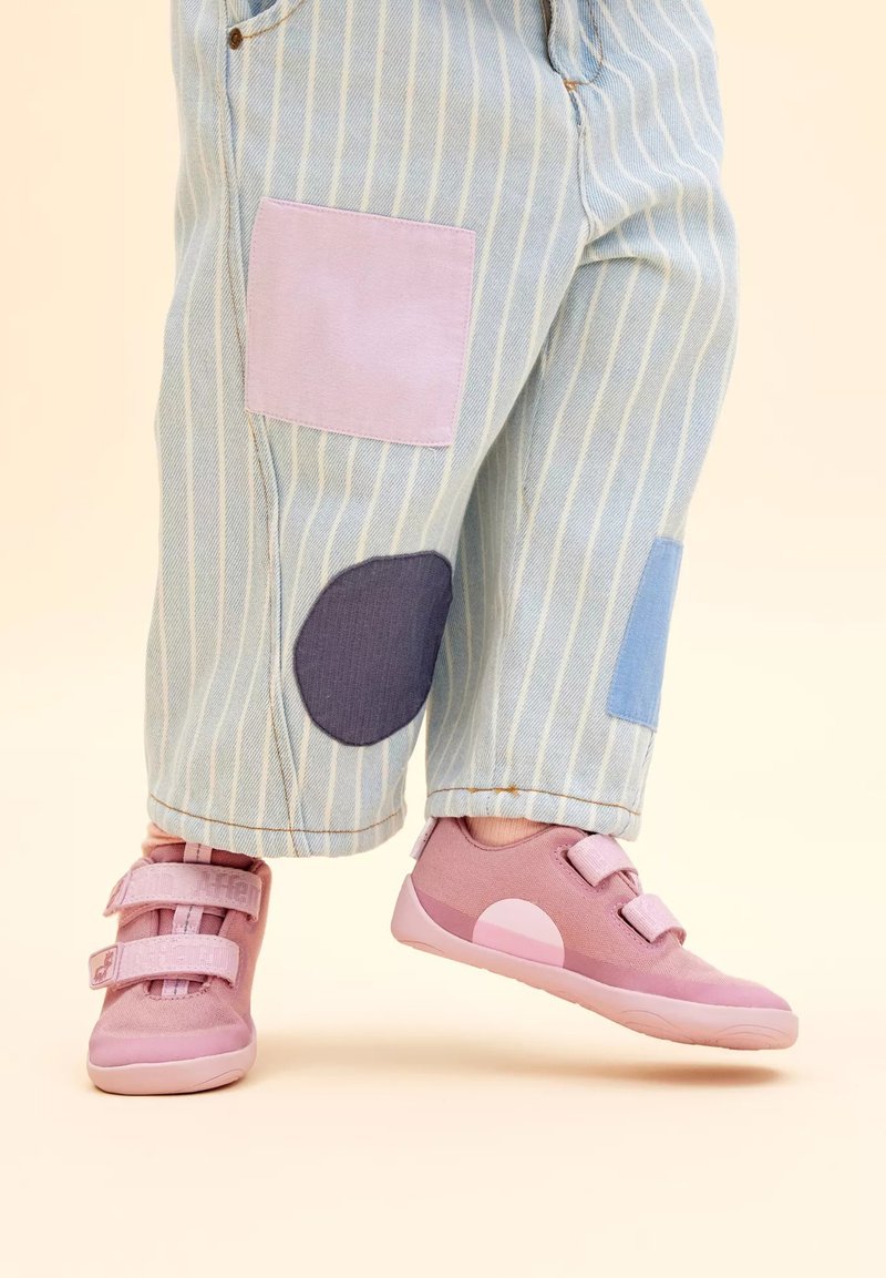 Roze sportieve schoenen met twee klittenbandsluitingen, gecombineerd met blauw gestreepte broek met lichtpaarse en donkerblauwe vlekken. Glad stoffen textuur.