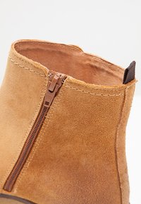 Stivale alla caviglia in suede marrone chiaro con una cerniera laterale, caratterizzato da una finitura testurizzata e una cucitura rinforzata lungo il bordo superiore.