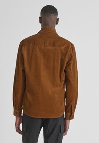 Bruine corduroy overhemd met een rechte snit, knopenmanchetten en een detail aan de achterzijde. Beschikt over een verticale ribbelstructuur en een gestikte zoom.