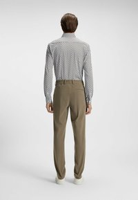 Langarmshirt met een zwart-wit patroon, gecombineerd met lichtbruine tapered pants en witte sneakers.