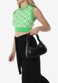Groen en crèmekleurig patroon crop top met een geribbelde halslijn, gecombineerd met hoge zwarte broeken. Een zwarte leren handtas met een gedraaide strap.