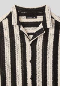 Camicetta a maniche corte a righe bianche e nere con colletto e chiusura a bottoni, realizzata in un tessuto testurizzato e traspirante.