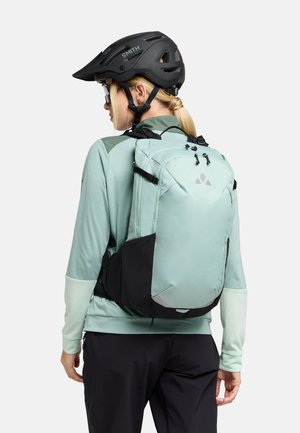 Zaino verde menta chiaro con dettagli neri, design aerodinamico, spallacci regolabili e dettagli riflettenti, indossato con un casco da ciclismo nero.