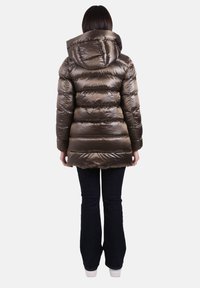 Gewatteerd jack in metallic brons, met een capuchon, doorgestikt ontwerp en lange mouwen. Gecombineerd met donkere uitlopende jeans en witte schoenen.