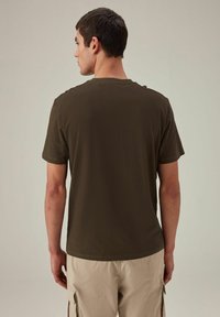 Barna rövid ujjú póló, kerek nyakkivágással, puha anyagból készült. A design egyszerű, egyenes vonalú, és nincsenek rajta látható márkajelzések.