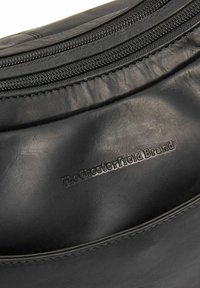 Zwarte leren tas met een gladde textuur, voorzien van een gebogen ontwerp, een ritsluiting en reliëfbranding van "The Chesterfield Brand."