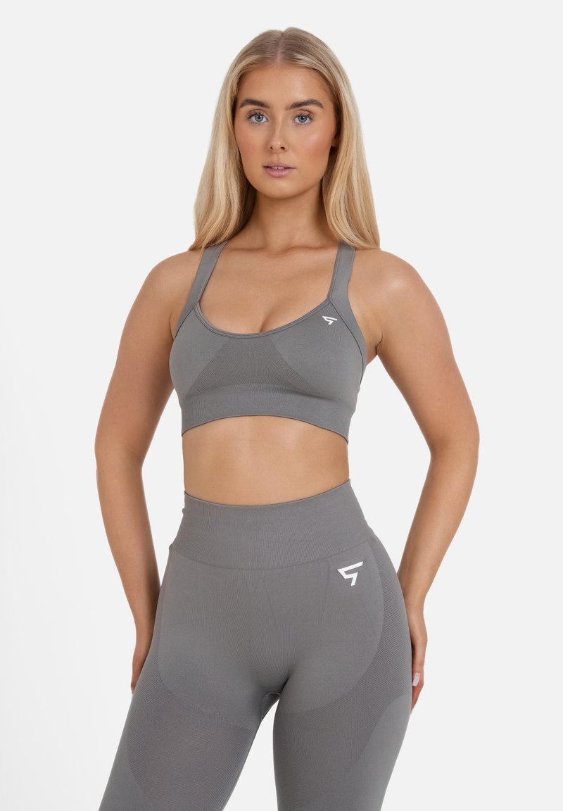 Grijze sportbeha met een gladde textuur en brede bandjes, gecombineerd met bijpassende high-waisted leggings met een subtiel patroon en logodetail.
