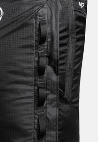 Svart ryggsäck med texturerad tyg med rutmönster, sidofästen i väv, och en zippered ficka för säker förvaring.