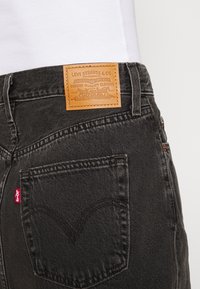 Zwarte denimjeans met een faux leren label met reliëfbranding, vijf-pocket ontwerp en rode tabdetails op de achterzak.
