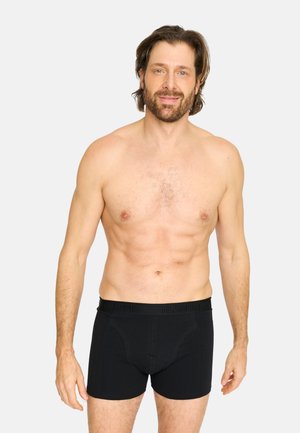 Sorte boxer briefs lavet af blødt stof med en bred talje, hvor mærket "CLAUDIO" er præget. Modellen står med afslappede arme.