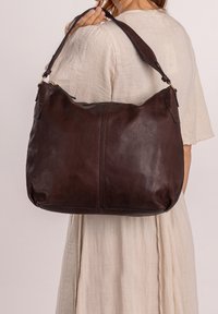 Grande borsa a spalla in pelle marrone con forma curva, texture liscia e tracolla regolabile con dettagli in metallo dorato.