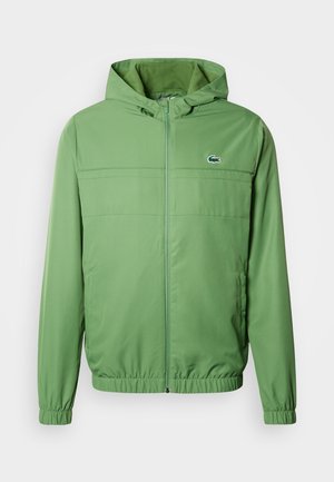 Zöld könnyű kapucnis dzseki cipzáras záródással, elasztikus mandzsettákkal és texturált mintázattal. Mellrészen kis logóval.