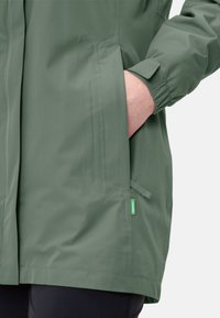 Grüne, leichte Jacke mit strukturierter Oberfläche, seitlichen Taschen, elastischen Bündchen und einem kleinen grünen Markenschild an der Naht.