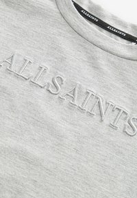 Pelēks treniņtērps ar apaļu kaklu, uz kura ir izcelta izšūta uzraksta "ALLSAINTS" gaismāk pelēkā krāsā, izgatavots no mīkstas auduma.