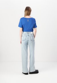 Camiseta de algodón azul con mangas cortas y cuello redondo. Jeans de cintura alta de un azul claro con detalles de tachuelas en los laterales y bolsillos de parche.