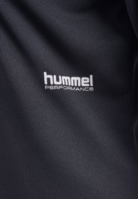 Zbliżenie czarnej tkaniny o fakturze z nadrukowanym białym logo „hummel PERFORMANCE”.