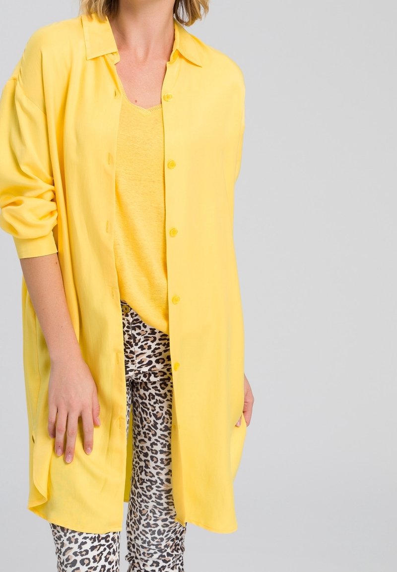 Chemise jaune à manches longues, avec une coupe décontractée et une texture douce, associée à un legging à imprimé léopard blanc et noir.