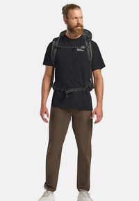 Sac à dos noir porté sur une chemise noire et un pantalon marron ; comprend des bretelles réglables, plusieurs poches et un design élégant.