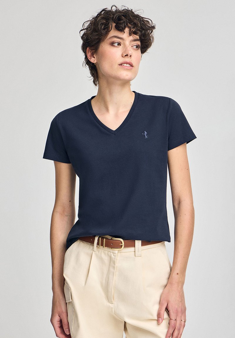 T-shirt a v in navy realizzato in cotone morbido, con maniche corte e un piccolo logo ricamato sul petto. Abbinato a pantaloni beige.