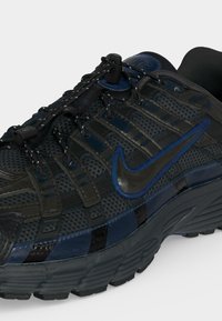 Μαύρο και σκούρο μπλε παπούτσι τρεξίματος Nike με επάνω μέρος από δίχτυ, διαμορφωμένη σόλα, ελαστικά κορδόνια και εμφανές λογότυπο Nike στο πλάι.