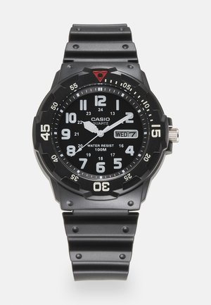 Schwarze Casio Quarz-Uhr mit rundem Gehäuse, leuchtenden weißen Ziffern, einem Datumsdisplay und einem strukturierten schwarzen Silikonarmband. Wasserdicht bis 100 m.