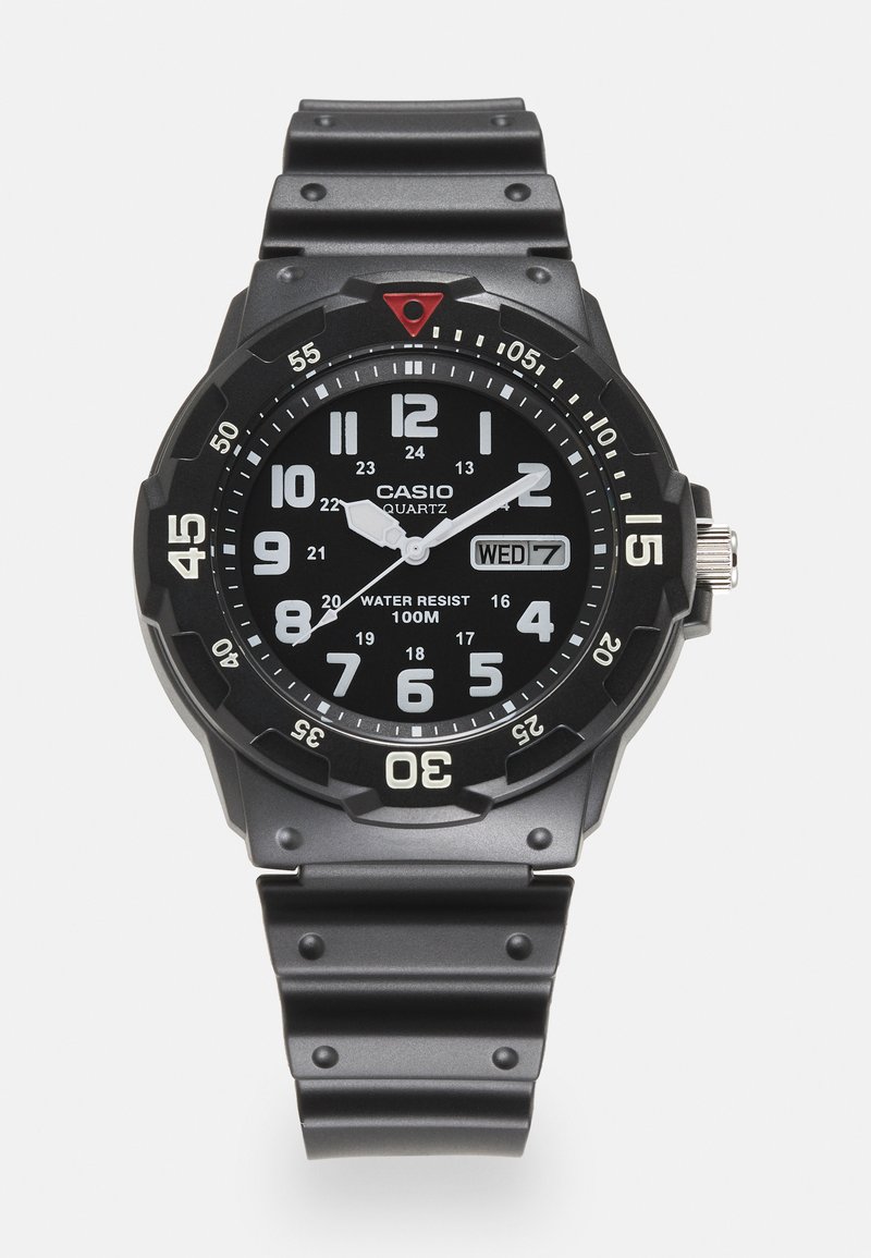 Montre quartz Casio noire avec un boîtier rond, des chiffres blancs lumineux, un affichage de la date et un bracelet en silicone noir texturé. Résistante à l'eau jusqu'à 100 m.