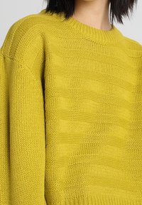 Pull en tricot jaune ornée d'un design texturé avec des rayures horizontales, un col rond et des manches longues. Fabriqué à partir d'un matériau doux et respirant.