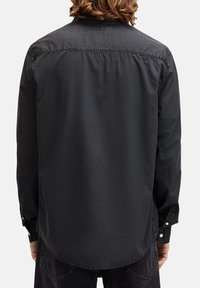 Camisa negra de manga larga hecha de tela ligera, con dobladillo curvo, puños abotonados y detalles de costura en la parte posterior.