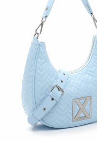 Sac à main matelassé bleu clair avec bandoulière ajustable, boucle argentée, fermeture éclair et plaque logo en métal à l'avant.