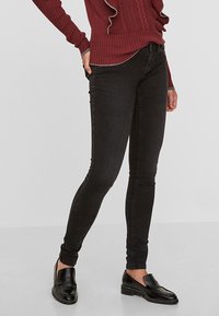 Jeans ajustados negros de denim, con una cintura de altura media, diseño tradicional de cinco bolsillos y un ligero desgaste en la tela.