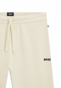 Pantalons de jogging texturés de couleur crème avec une taille élastique réglable. Présente un logo "BOSS" en broderie noire sur la jambe inférieure.