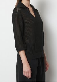 Czarny dziany sweter z dekoltem w serek i kołnierzykiem; ma luźny, otwarty splot oraz rękawy o długości trzech ćwiartek z prążkowanym wykończeniem.