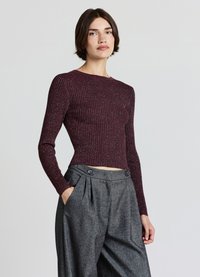 Bordeauxrotes, geripptes Langarmshirt mit rundem Ausschnitt, kombiniert mit hoch taillierter grauer Hose mit Plisseefalten und aufgesetzten Taschen vorne.