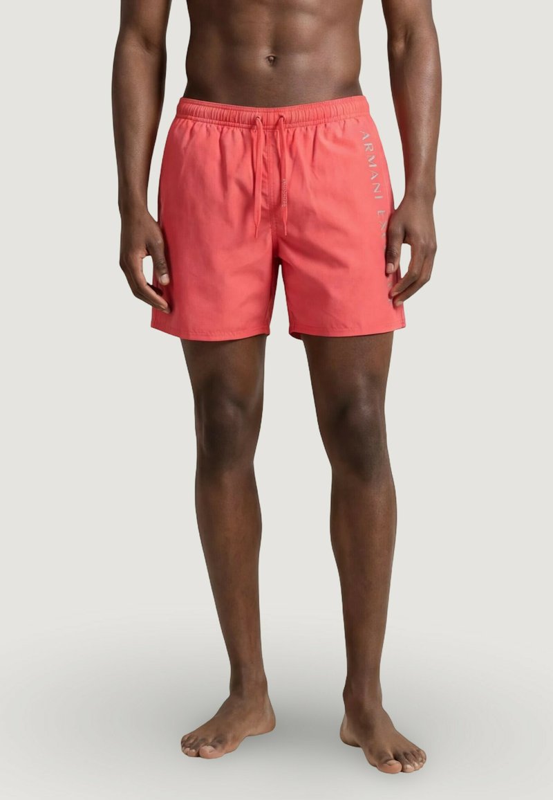 Homme portant un short de bain corail rose mi-cuisse avec cordon de serrage réglable et logo "Armani Exchange" sur la jambe gauche.